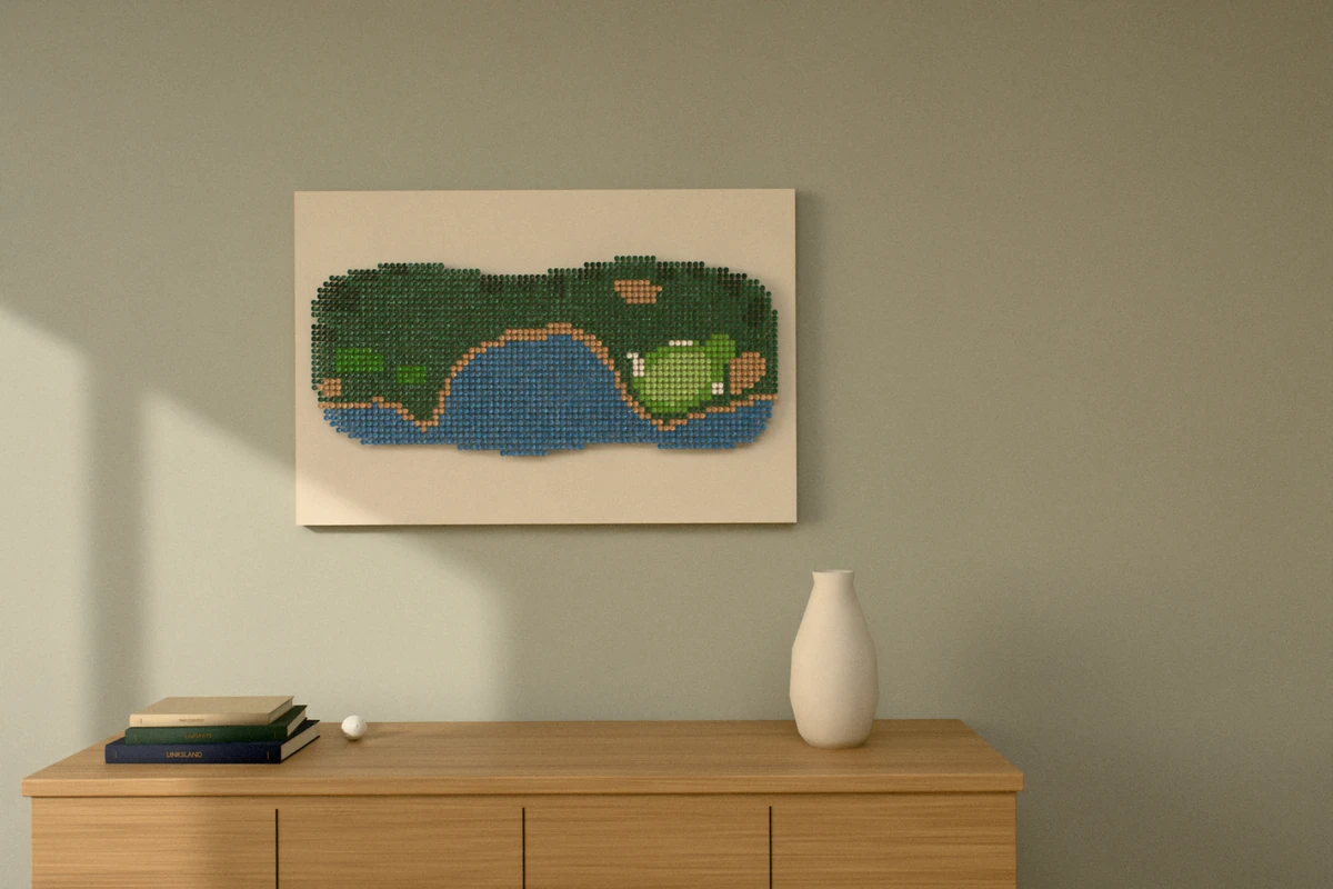 A golf-tee picture of a par 3 played across an ocean cove, hung wide on a sage wall above a wooden sideboard with books and a vase.